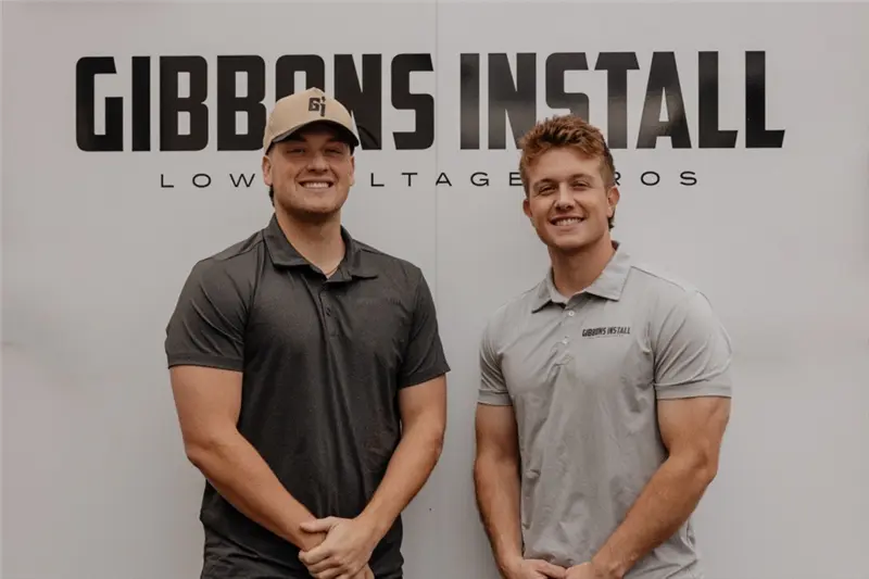 Two Gibbons team members in front of the Gibbons Install sign